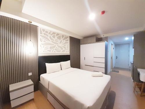 a bedroom with a large white bed and a desk at Modern Classic Studio at Mataram City Apartment By Travelio in Kejayan