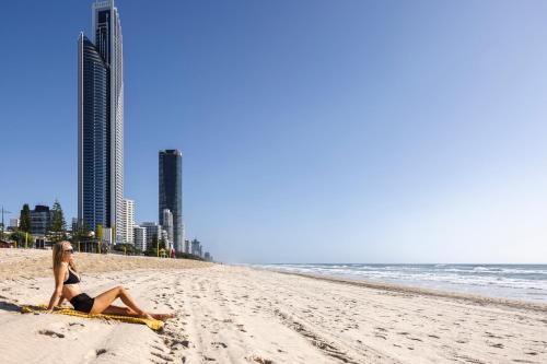 a woman sitting on a surfboard on a beach at The Shores Surfers Paradise Apartments in Gold Coast