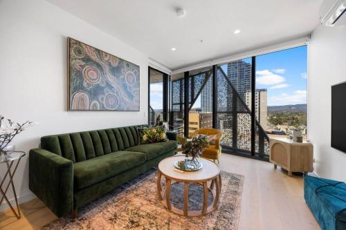 a living room with a green couch and large windows at Skyline Retreat - 2BR Luxury City Apartment in Adelaide