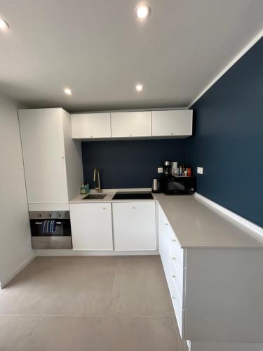 a kitchen with white cabinets and a blue wall at Èze - Appartement dans bas de villa avec piscine près de Monaco in Èze