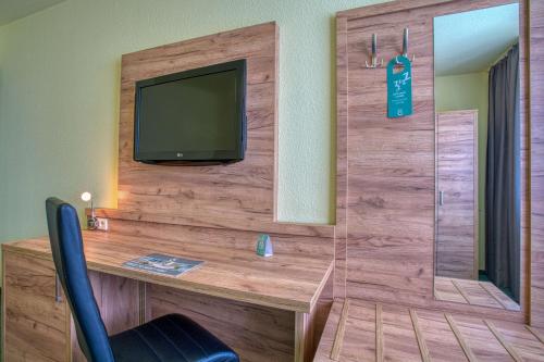 a room with a desk with a television on a wall at Centro Hotel Böblingen, Trademark Collection by Wyndham in Böblingen