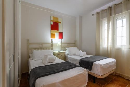 2 Betten in einem Zimmer mit weißen Wänden und Fenstern in der Unterkunft Marina III PLUS by Ĥ - Marina Isla Canela PMHIII6P18 in Punta del moral