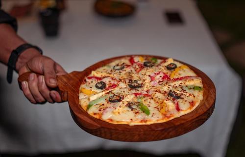 a person holding a pizza in a wooden bowl at Nazaara - A Luxe Retreat in Manāli