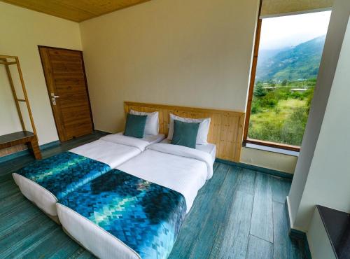 a bedroom with a large bed with a large window at Nazaara - A Luxe Retreat in Manāli