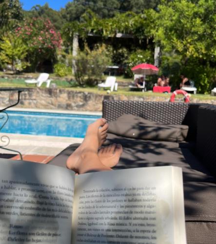 a book with a persons feet on a chair with a pool at Rural Coliving in Pontevedra