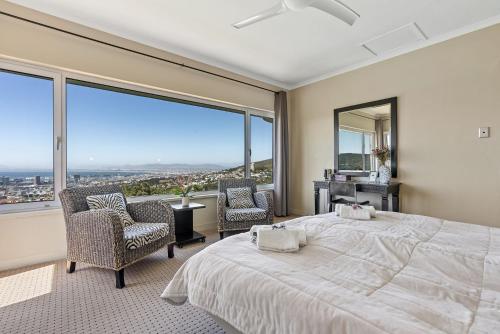 a bedroom with a bed and two chairs and a large window at Villa Blue Sky Cape Town in Cape Town
