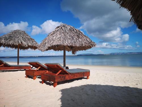 two straw umbrellas and lounge chairs on a beach at Hotel Lakana Ramena in Diego Suarez