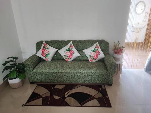 a green couch with three pillows on it in a living room at Greenwood Cabins Homestay, The Greenhouse in Jorhāt