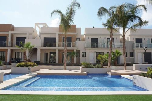 a swimming pool in front of a building with palm trees at Duplex Zenia beach, La zenia in Playa Flamenca