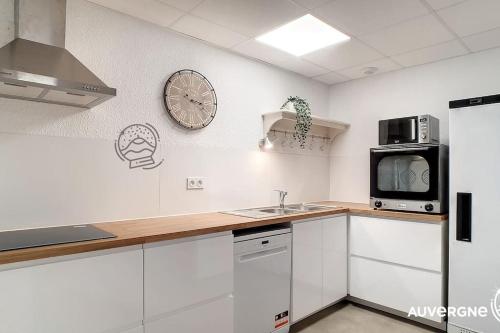 une cuisine avec des placards blancs et une horloge murale dans l'établissement Le Poulailler, à Murol