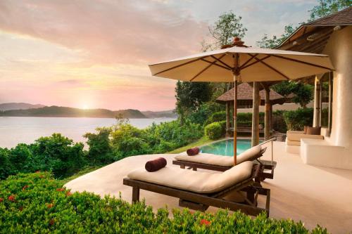 a resort with a pool and two lounge chairs and an umbrella at The Naka Island, a Luxury Collection Resort & Spa, Phuket in Ko Naka