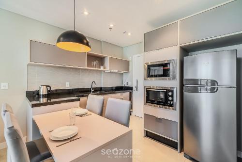 a kitchen with a table and a stainless steel refrigerator at MHF II - Apts Variados em Prédio com Vista para o Mar em Itapema in Itapema