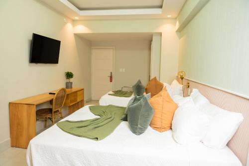 two beds in a room with a desk and a television at Hotel Stay Here Suites in Santo Domingo