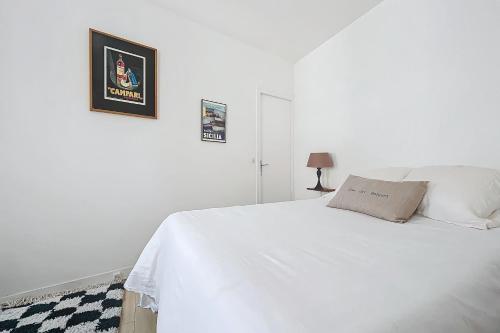 - un lit blanc dans une chambre blanche avec une photo sur le mur dans l'établissement Cozy Studio in the Heart of Oberkampf, à Paris