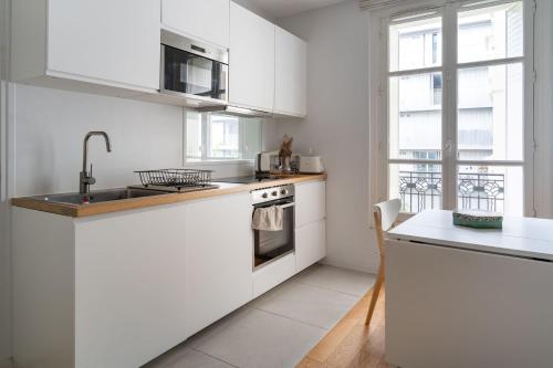 une cuisine avec des armoires blanches, un évier et une fenêtre dans l'établissement Airy and Stylish 1BD Flat ile Saint-Louis, à Paris