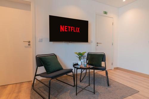 two chairs and a table with a television on a wall at 7Min to Uni Sé-Velha - AC - Work Desk - 300MBs WiFi - Suite 5 in Coimbra