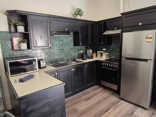 a kitchen with black cabinets and a stainless steel refrigerator at Charming! 3 Bed Garden by Beach in Largs