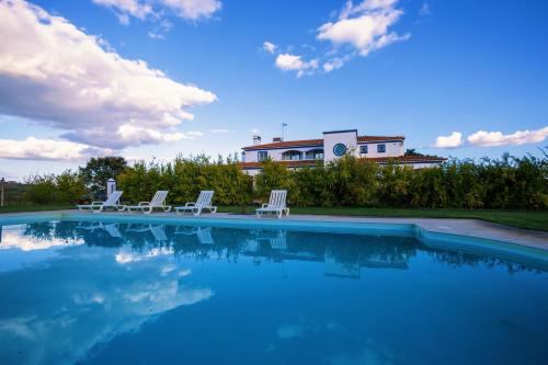 a swimming pool with two chairs and a house at Herdade Dos Barros in Terena