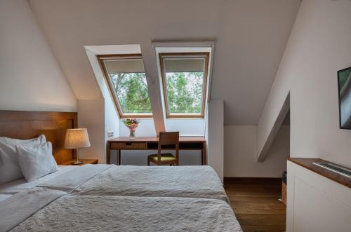 a bedroom with a bed and a desk and two windows at Tisza Balneum Hotel in Tiszafüred