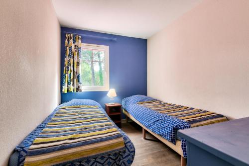 Cette chambre comprend 2 lits dans une chambre dotée de murs bleus et d'une fenêtre. dans l'établissement Les Maisons de Lacanau les Pins - maeva Home - Maisons 3 pièces 6 personnes - Prestige MAE-4591, à Lacanau