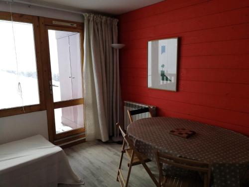 Cette chambre rouge comprend une table, un lit et une fenêtre. dans l'établissement Résidence Les Gentianes - Résidence LES GENTIANES N°F18 MAE-4741, à La Plagne Tarentaise