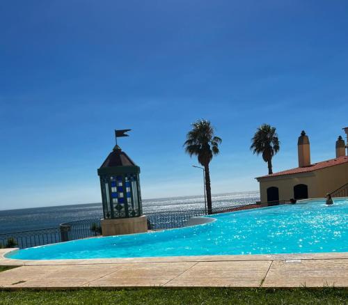 a swimming pool with a lighthouse and palm trees at Beachfront apartment with a pool- Parede in Parede