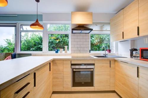 a large kitchen with wooden cabinets and windows at Stylish quiet garden flat with parking in London Zone 4 in Bromley