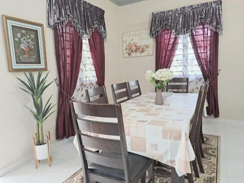 comedor con mesa, sillas y cortinas rojas en Homestay Bajet Machang - Lycaste, en Kampong Batu