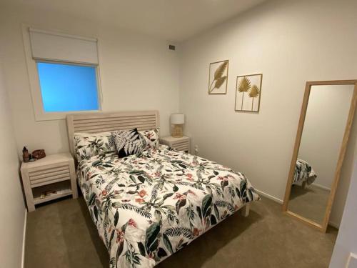 una camera da letto con un letto con un piumone floreale e uno specchio di Sunset Apartment, Mount views, POOL, GYM, HOT TUB a Mount Maunganui