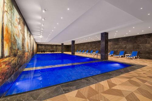 a pool with blue water in a room with blue chairs at Ramada by Wyndham Gaziantep in Gaziantep
