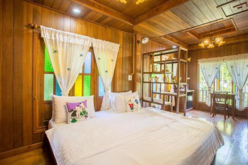 a bedroom with a white bed with wooden walls and windows at Suksatan Lamphun in Lamphun