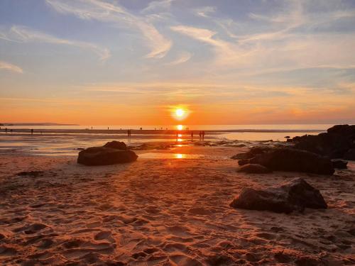 a sunset on a beach with rocks in the sand at Tehidy Holiday Park in Illogan