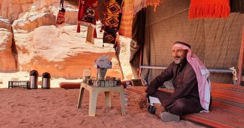 a man sitting on a bed next to a table at Dream Bedouin Life Camp Wadi Rum in Disah