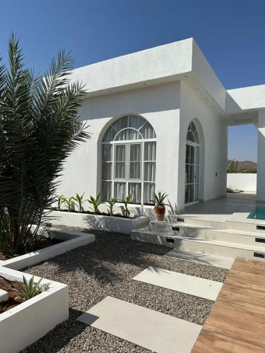a white house with a palm tree in front of it at Wadi Bani Khalid - Al Joud Green Hostel 2 in Dawwah