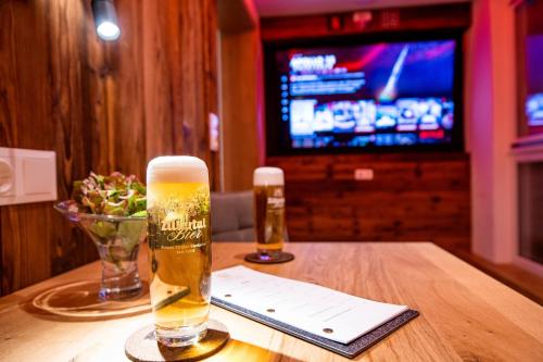 two glasses of beer on a wooden table with a television at Alpenhof Hotel Garni Suprême in Zell am Ziller