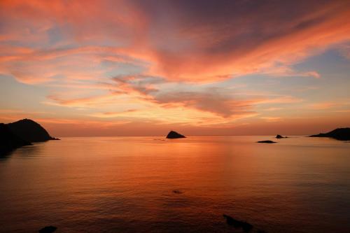 a sunset over the ocean with rocks in the water at 海の陽 in Nonami