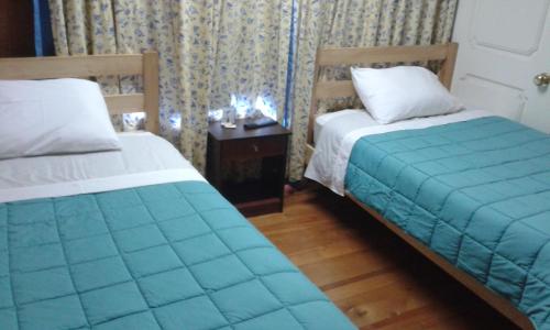a bedroom with two beds and a table with a night stand at Hostal Kutralwe in Pucón
