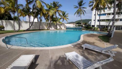 a swimming pool with two lounge chairs and palm trees at Hermoso Apto Playero con Piscina in Cumaná