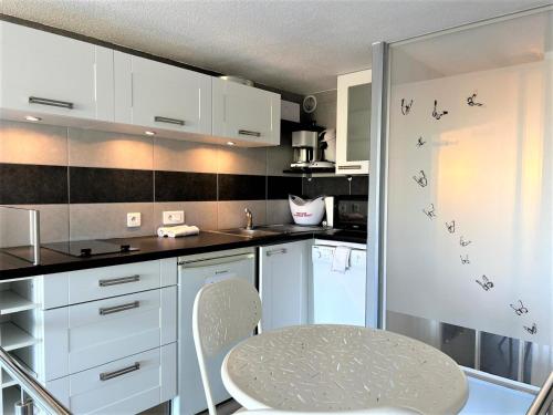 une cuisine avec des armoires blanches et une table à l'intérieur dans l'établissement Beau studio sur coursives à Port Nature au village naturiste, au Cap d'Agde