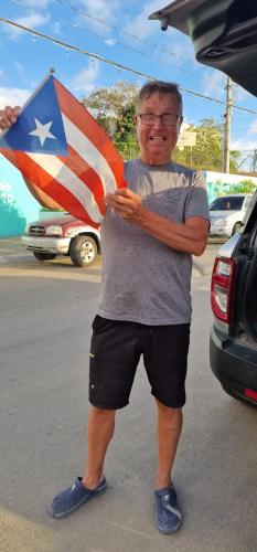a man standing next to a car with an american flag at Rooster Run Camping is a - rooftop & elevated camping experience! Incredible views of The Rain Forrest and Culebra across the Atlantic Ocean - Tents, towels, comfortable Air Beds, Warm Shower-Central Location- 5 beaches -25 min walk & Ferry is 20 min in Vieques