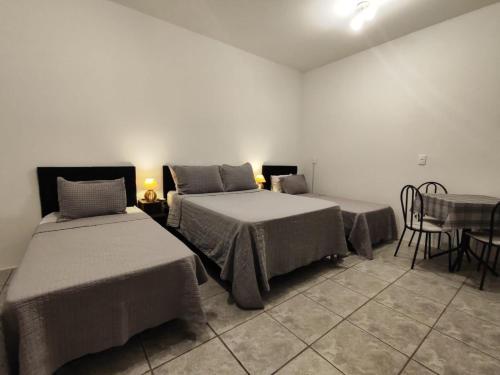 two beds in a room with a table and chairs at Villa Bilac - Amplos Studios 2km da Vila Germânica in Blumenau