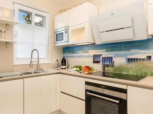 a kitchen with white cabinets and a painting of the beach at Holiday Home Traumzeit II in Zingst