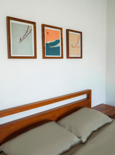 three framed pictures on a white wall above a bed at Rumah Markisa Batukaras in Batukaras