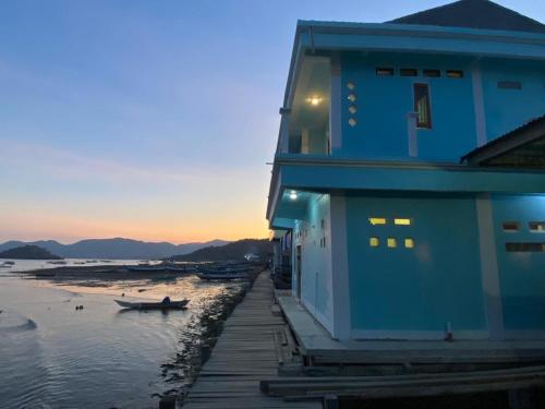 a blue building with a boat on the beach at Komodo Homestay in Komodo