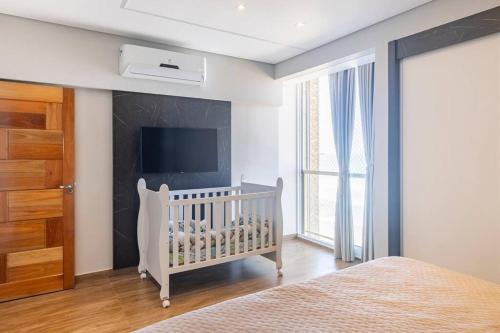 a white crib in a bedroom with a tv at Apartamento pe na areia nas pitangueiras in Guarujá
