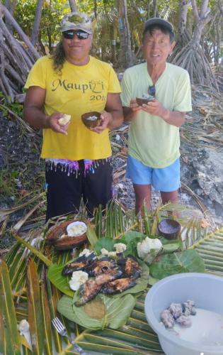 two people standing in front of a table of food at Penu Maurua 1 in Te-Fare-Arii