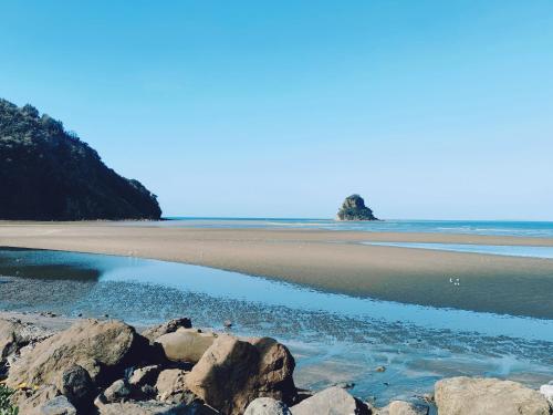 a beach with rocks in the sand and water at Orewa New house with view on deck near Cafe,bush & river in Orewa