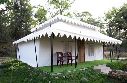 a white tent with two chairs in the grass at Woods Creek in Dandeli