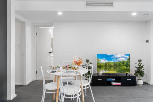a white dining room with a table and a tv at Apt Near Garden City&3km to QSAC in Brisbane