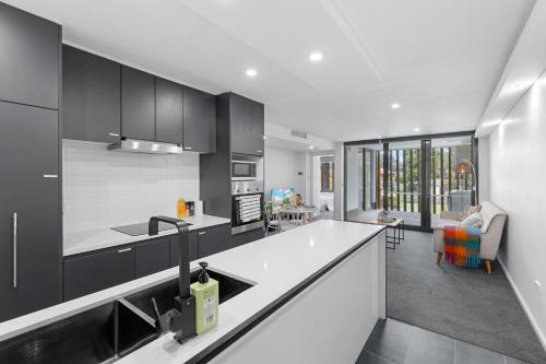 a kitchen with black and white cabinets and a living room at Apt Near Garden City&3km to QSAC in Brisbane